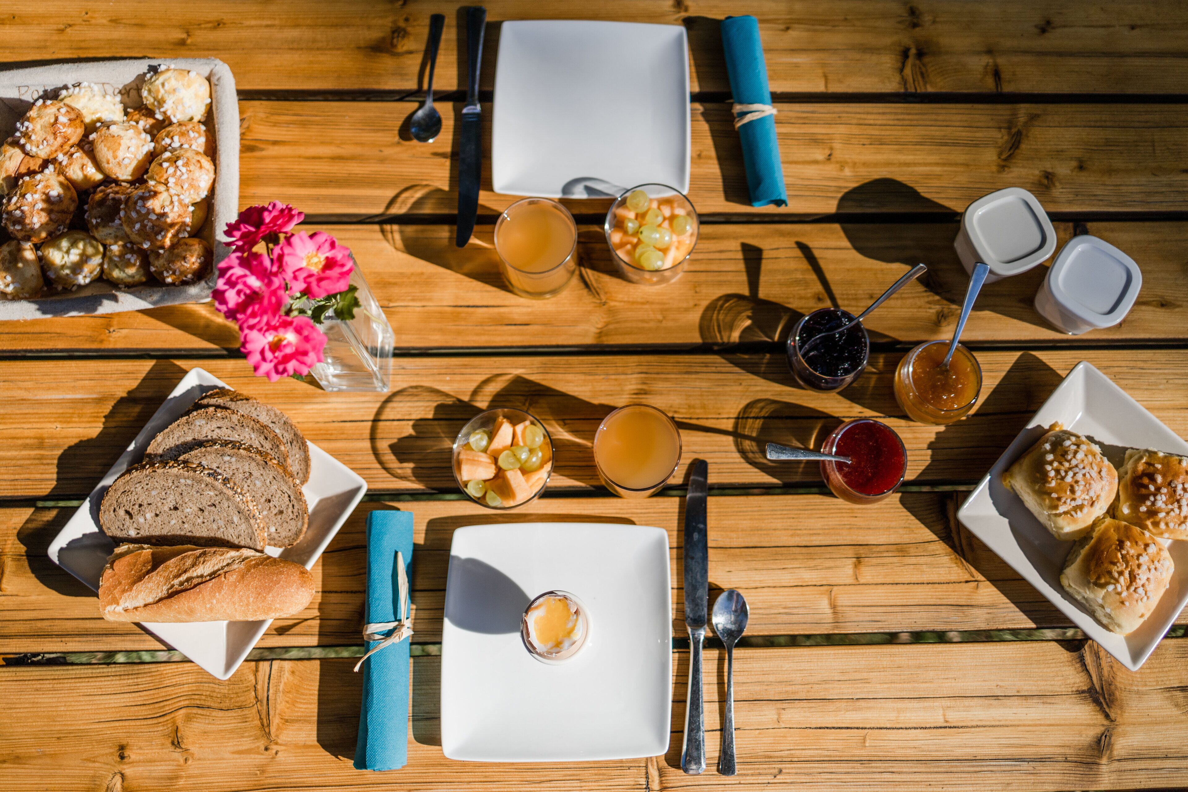 A wooden table with various food items, including bread, pastries, and fruits, along with glasses of beverages.