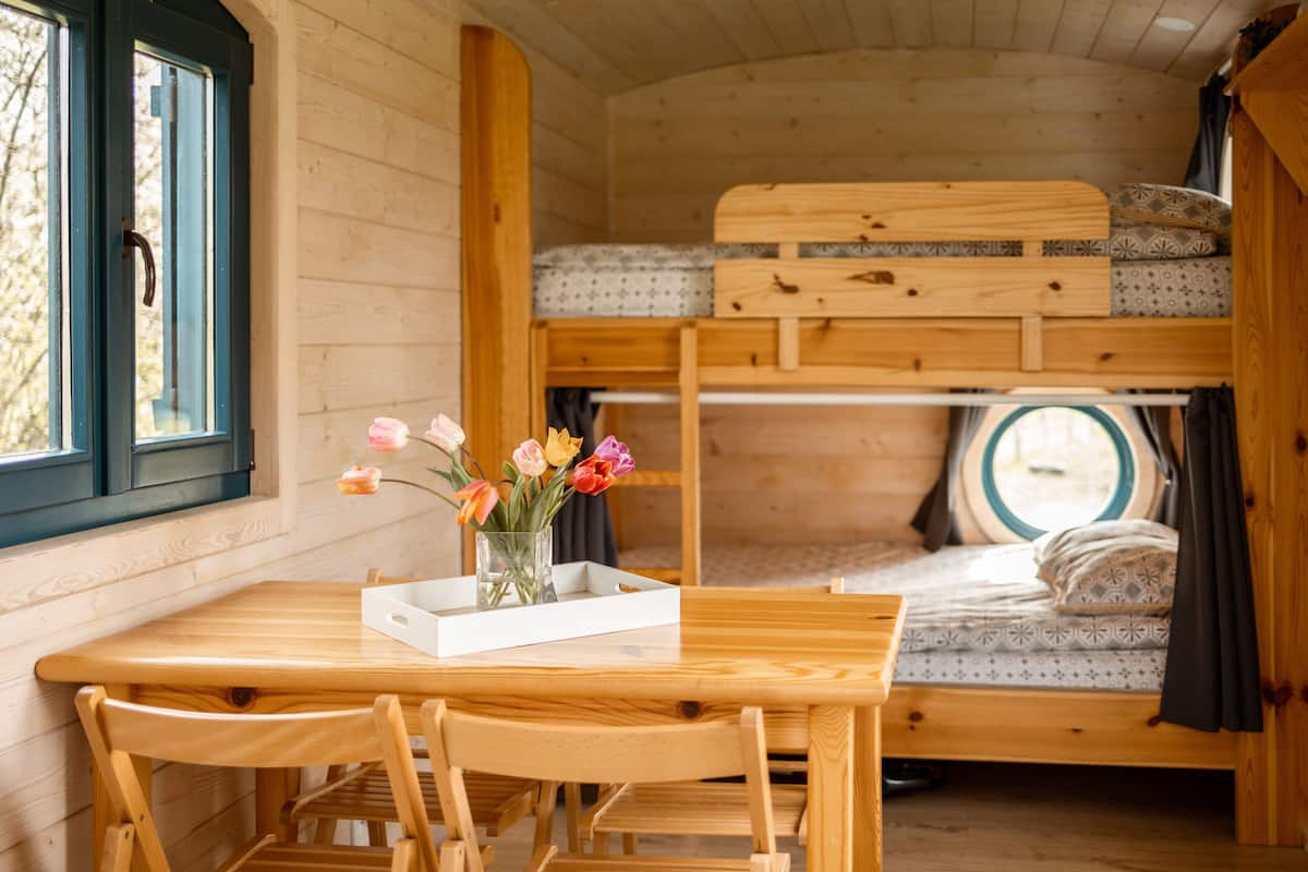 Un interior de madera con una litera, una mesa con sillas y un jarrón con flores.