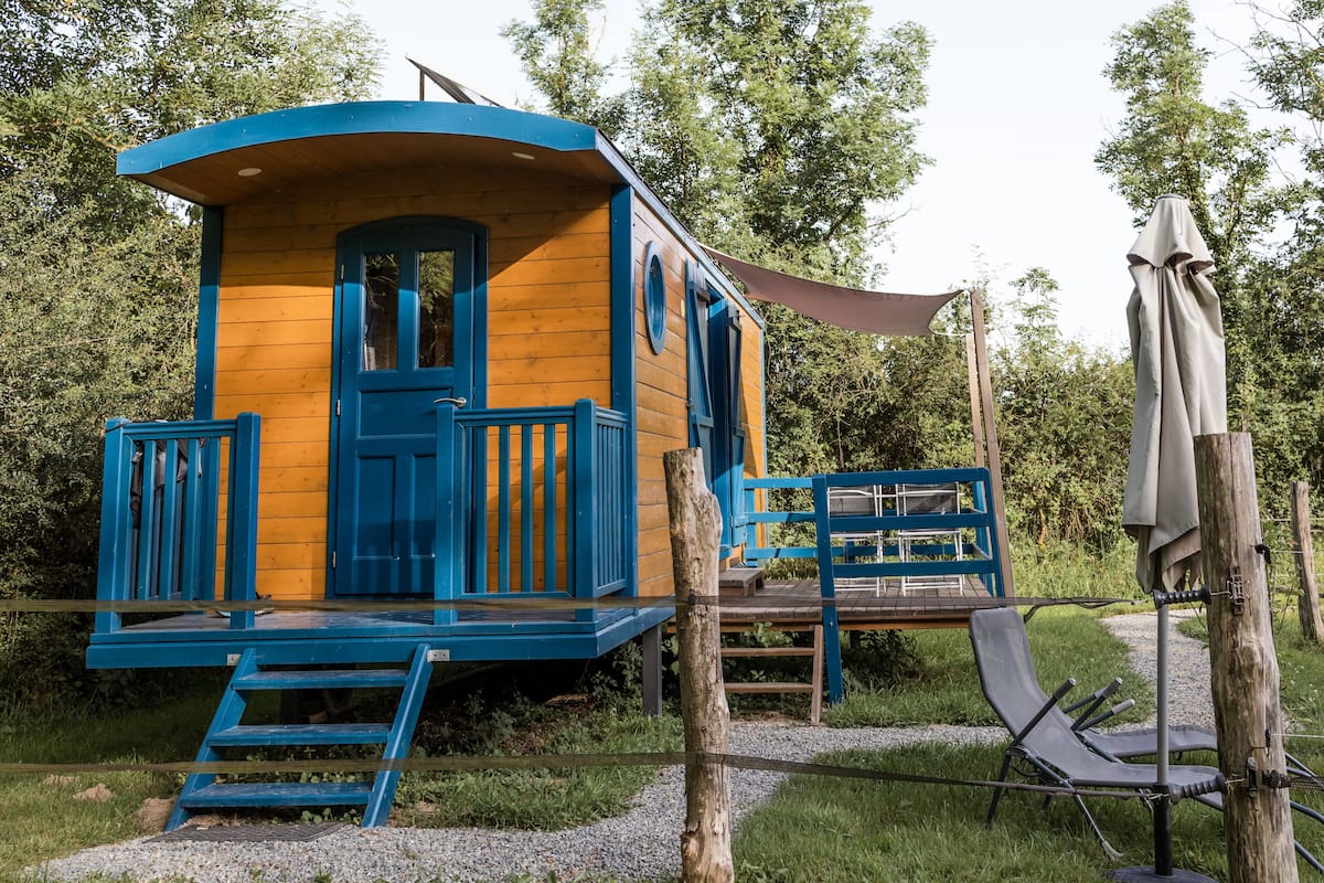 Una cabaña de madera con fachada azul, una puerta principal y un pequeño porche con un banco.