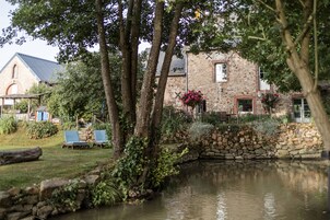 Un edificio de piedra con un estanque, rodeado de árboles y un pequeño jardín.