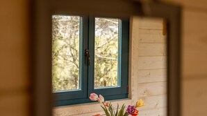 Un miroir reflétant une fenêtre donnant sur des arbres, une table en bois avec un vase de fleurs et un mur en bois.