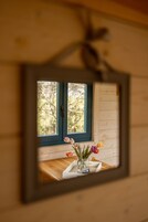 Un espejo refleja una ventana con vistas a árboles, una mesa de madera con un florero y una pared de madera.