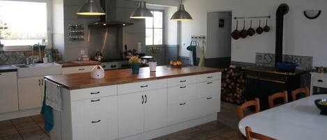 A modern kitchen with white cabinetry, a wooden island, pendant lighting, and a dining area with wooden chairs.