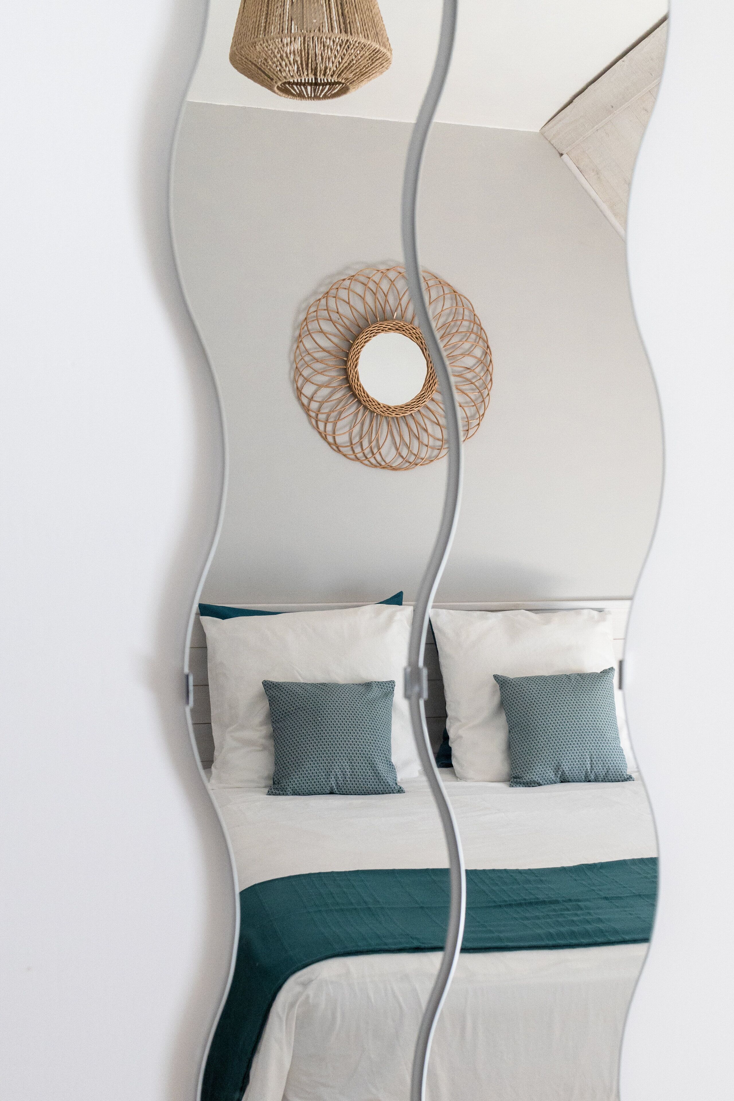 A bed with white and teal bedding, a woven wall hanging, and a single light fixture.