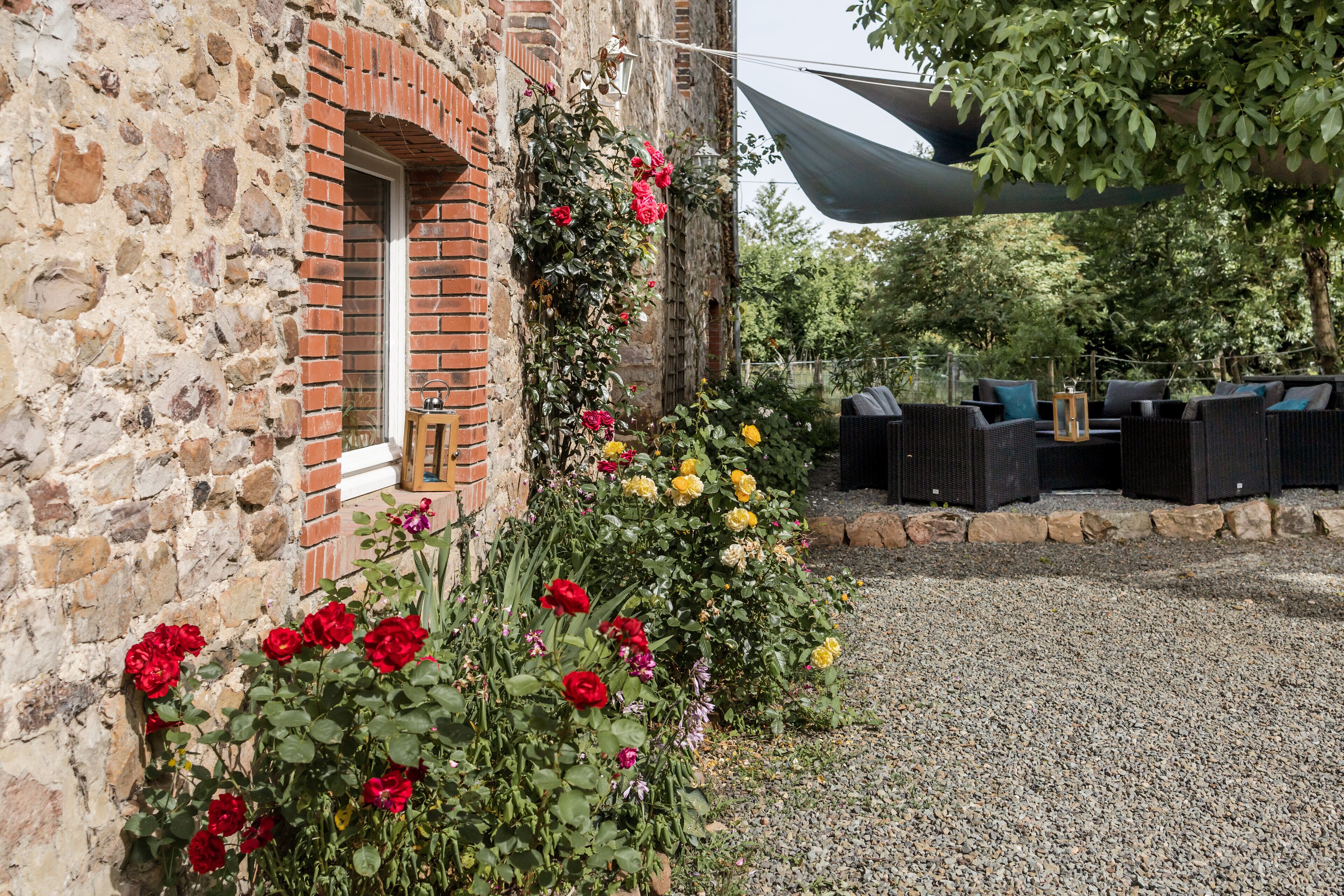 Un bâtiment en pierre avec une fenêtre en briques, une terrasse en gravier et des sièges d’extérieur avec des coussins.
