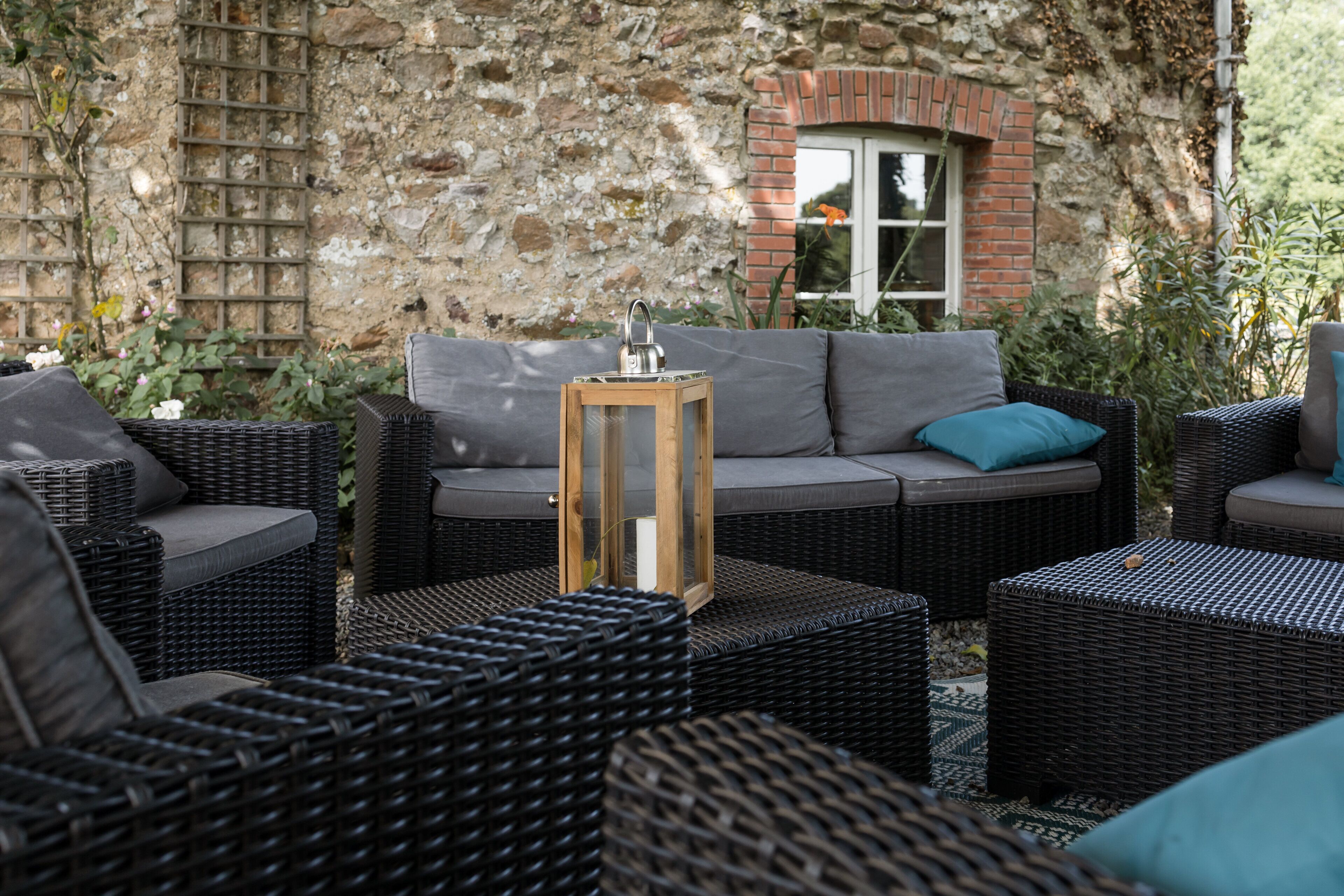 A wicker outdoor seating area with a cushioned sofa and a lantern.