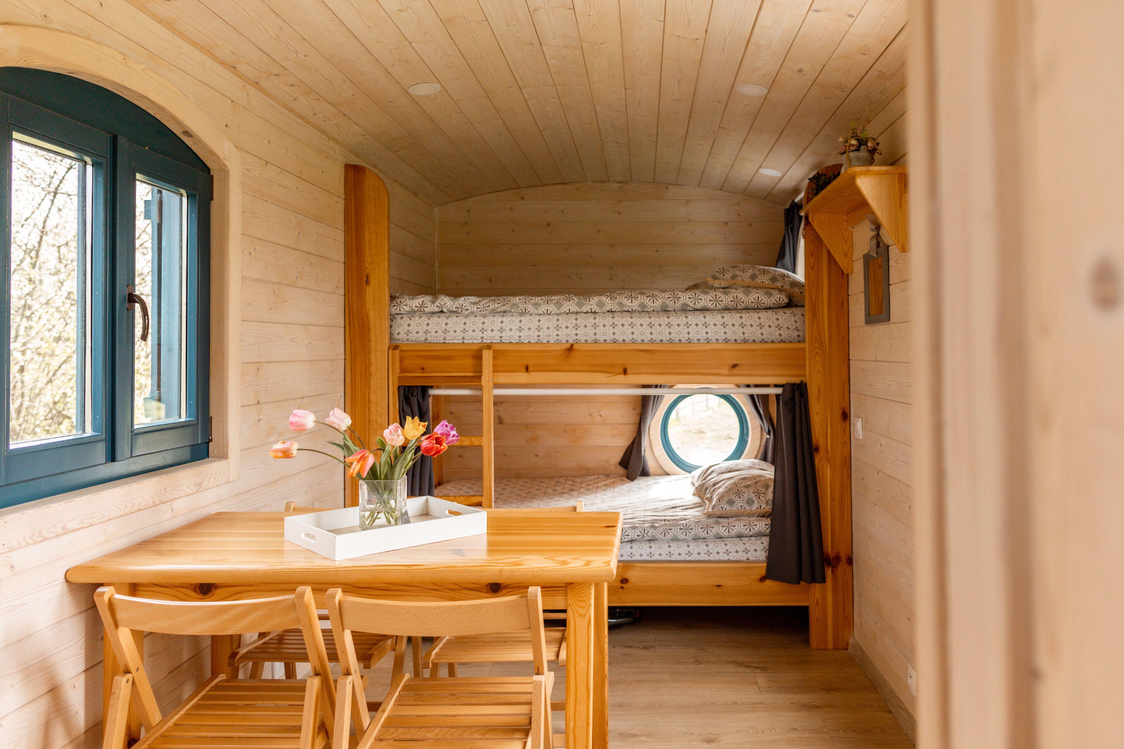 Ein gemütliches Holzhaus mit Hochbett, Esstisch und Stühlen sowie einem Fenster mit Vorhängen.