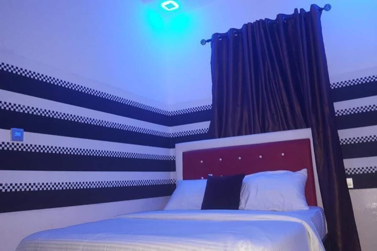 A bedroom with a checkered wall pattern, a bed with white and dark pillows, and a red headboard.