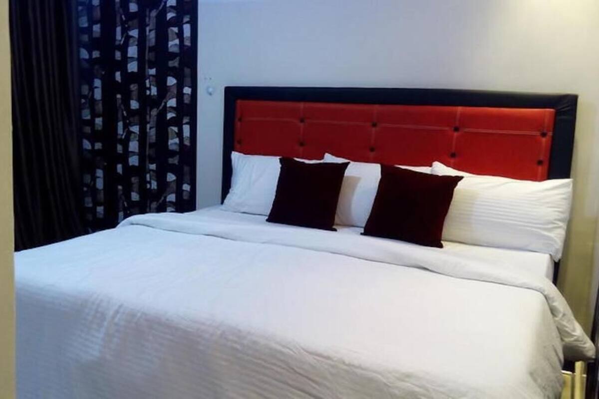 A hotel room with a bed, white bedding, and a red headboard.