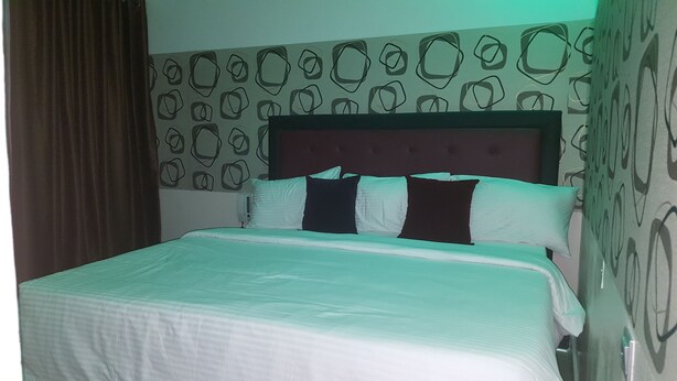 A neatly made bed with a white comforter and several pillows, a headboard with a tufted design, and a wall with a geometric pattern. - Nero Hotel (Lekki)