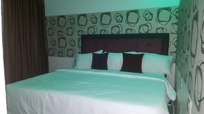 A neatly made bed with a white comforter and several pillows, a headboard with a tufted design, and a wall with a geometric pattern. - Nero Hotel (Lekki)