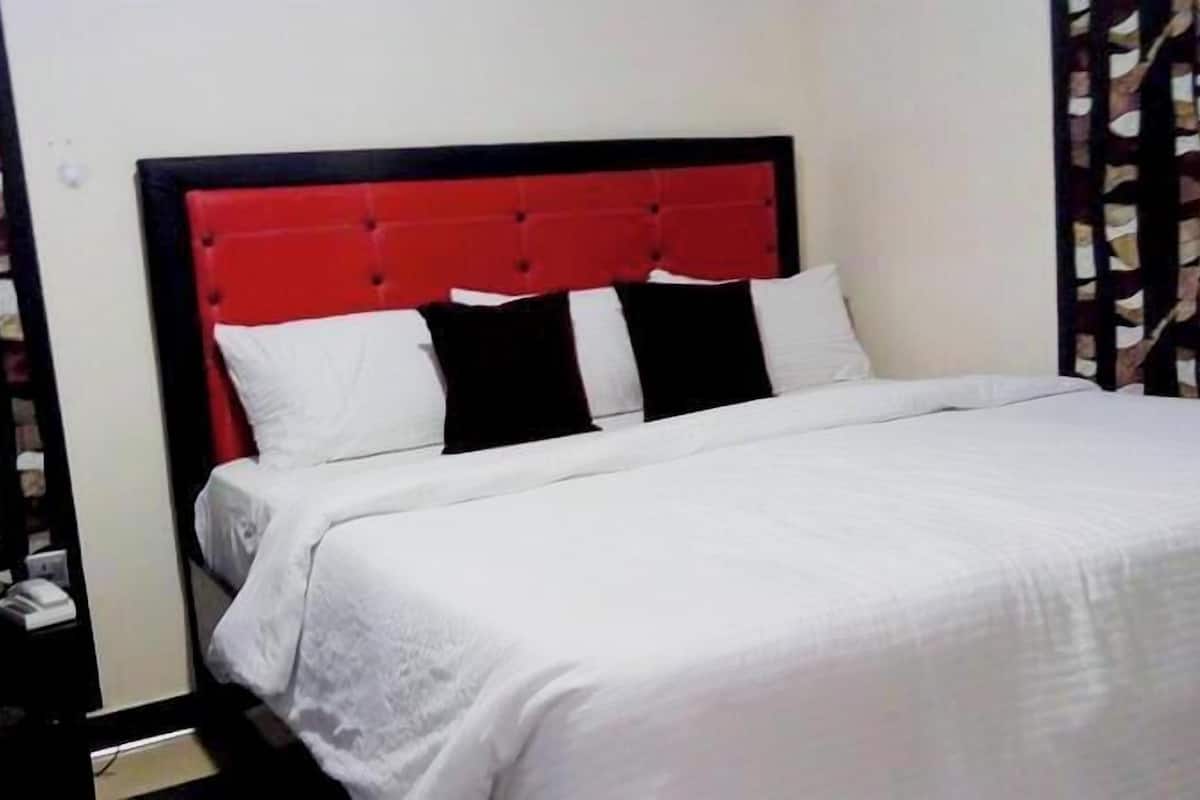 A bed with a red headboard, white bedding, and black pillows.