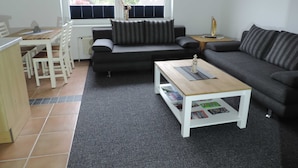 A modern living room with a grey sofa, a wooden coffee table, and a dining area with a white table and chairs.
