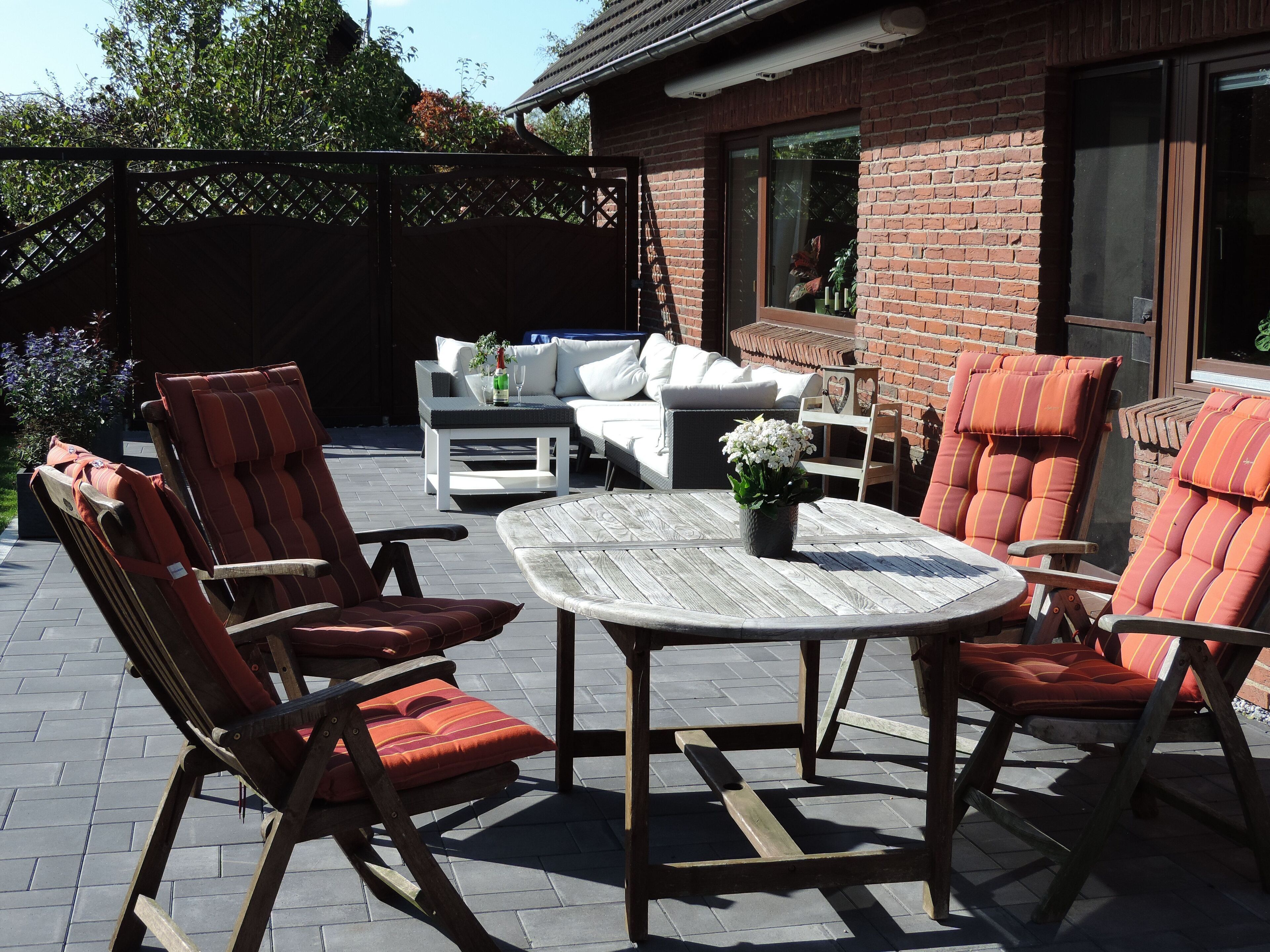 An outdoor patio area with a round wooden table, cushioned chairs, and a sofa.