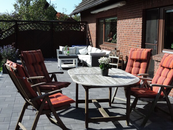 An outdoor patio area with a round wooden table, cushioned chairs, and a sofa.