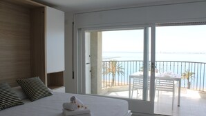 A hotel room with a large bed, a balcony with a view of the sea, and a dining area with a table and chairs. - Pi Sunyer 4 1B - One Bedroom Apartment, Sleeps 4 (Roses)