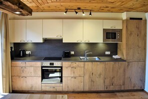 A modern kitchen with wooden cabinets, a built-in oven, a microwave, and a sink. - Alpenrose - Wiesenhof (Kaunerberg)