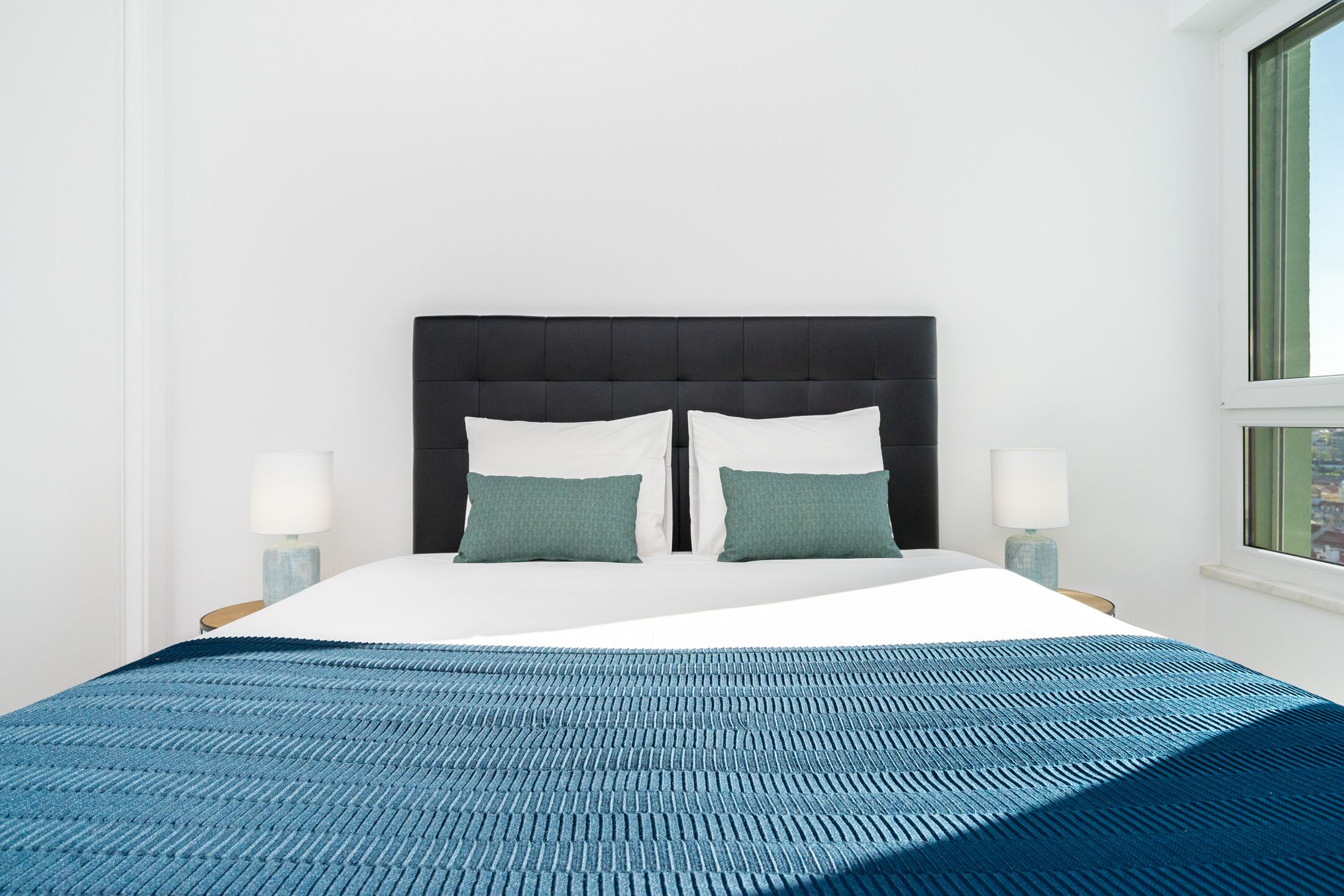 A bed with a dark headboard, two pillows, and a blue textured bedspread.