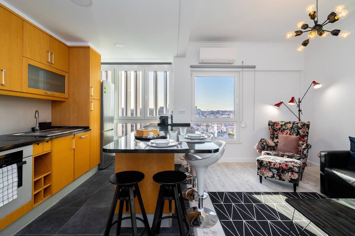 Eine moderne Küche mit einer zentralen Kochinsel, Barhocker und einem großen Fenster mit Blick auf die Stadt.