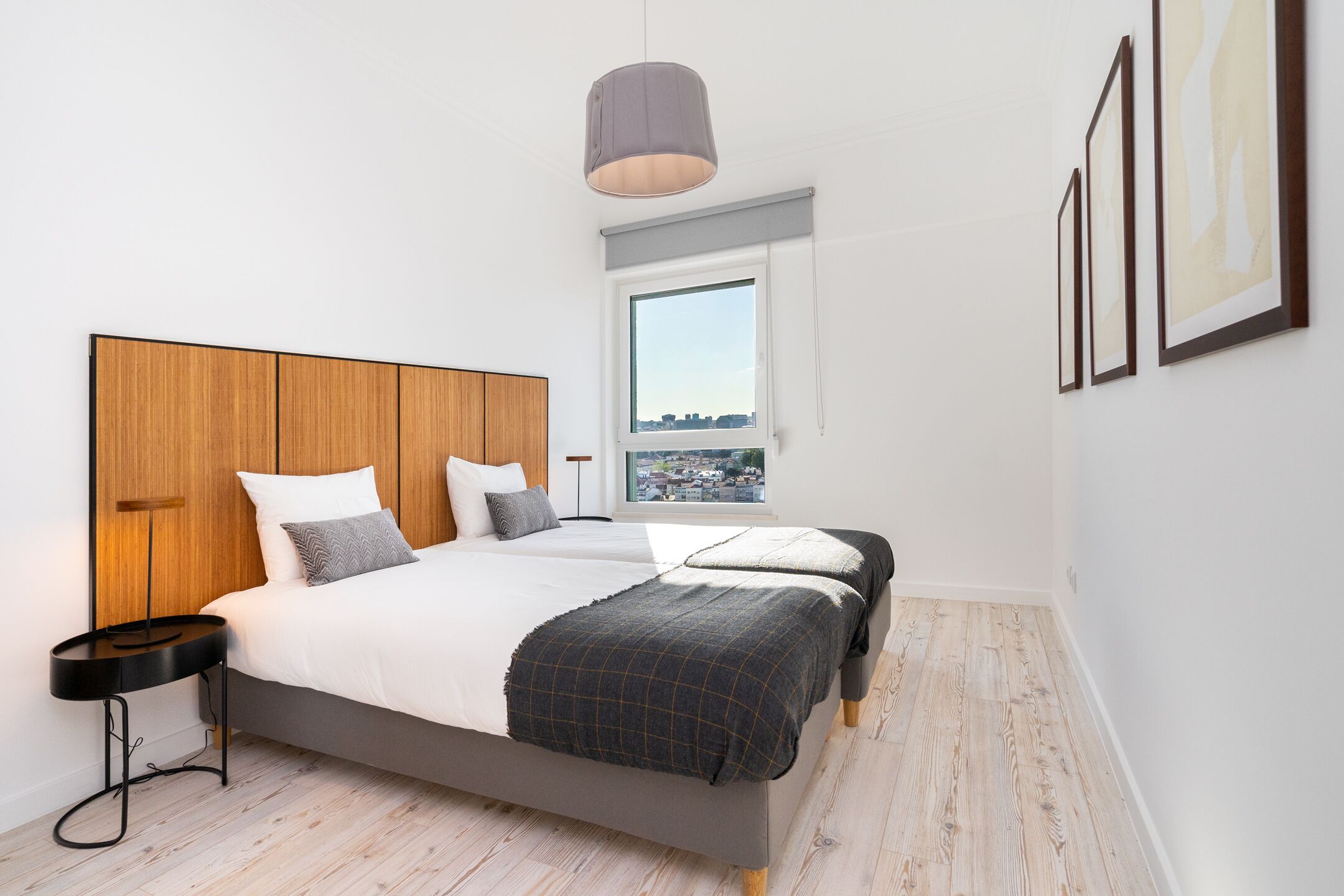 Un dormitorio moderno con una cama grande, una mesita de noche, una ventana con vista a la ciudad y obras de arte enmarcadas en la pared.