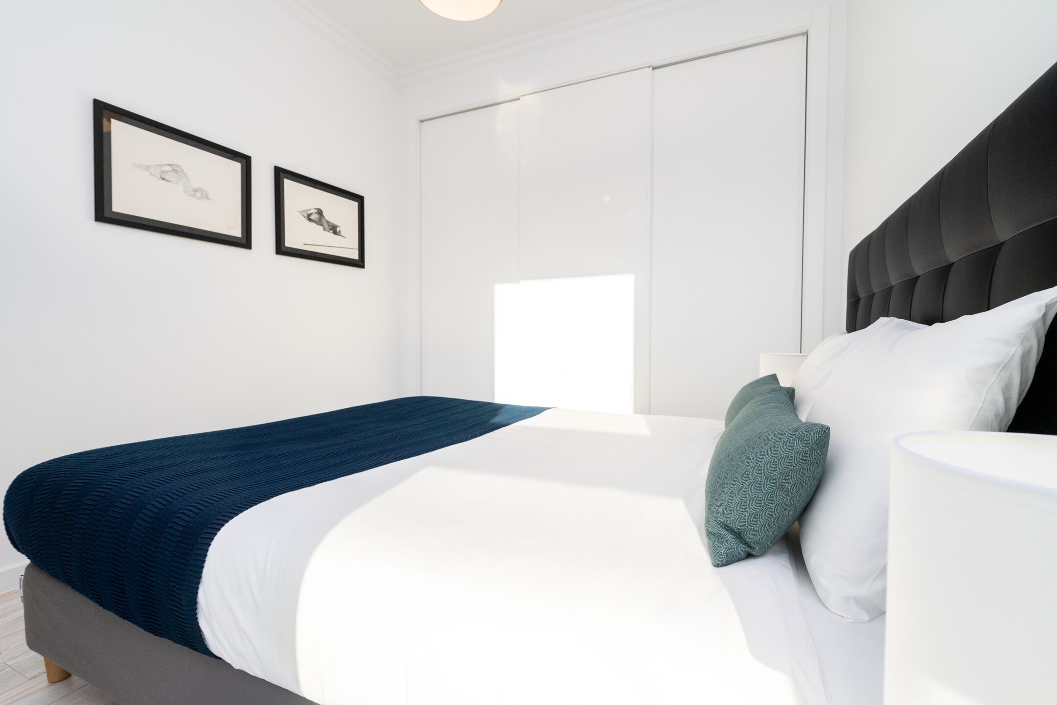 A modern bedroom with a bed, white walls, and two framed pictures.