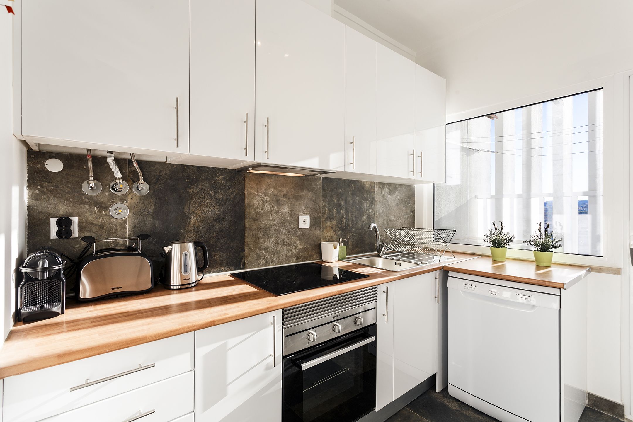 Een moderne keuken met witte kastjes, een zwart aanrecht, een ingebouwde oven, een vaatwasser en een raam voor natuurlijk licht.