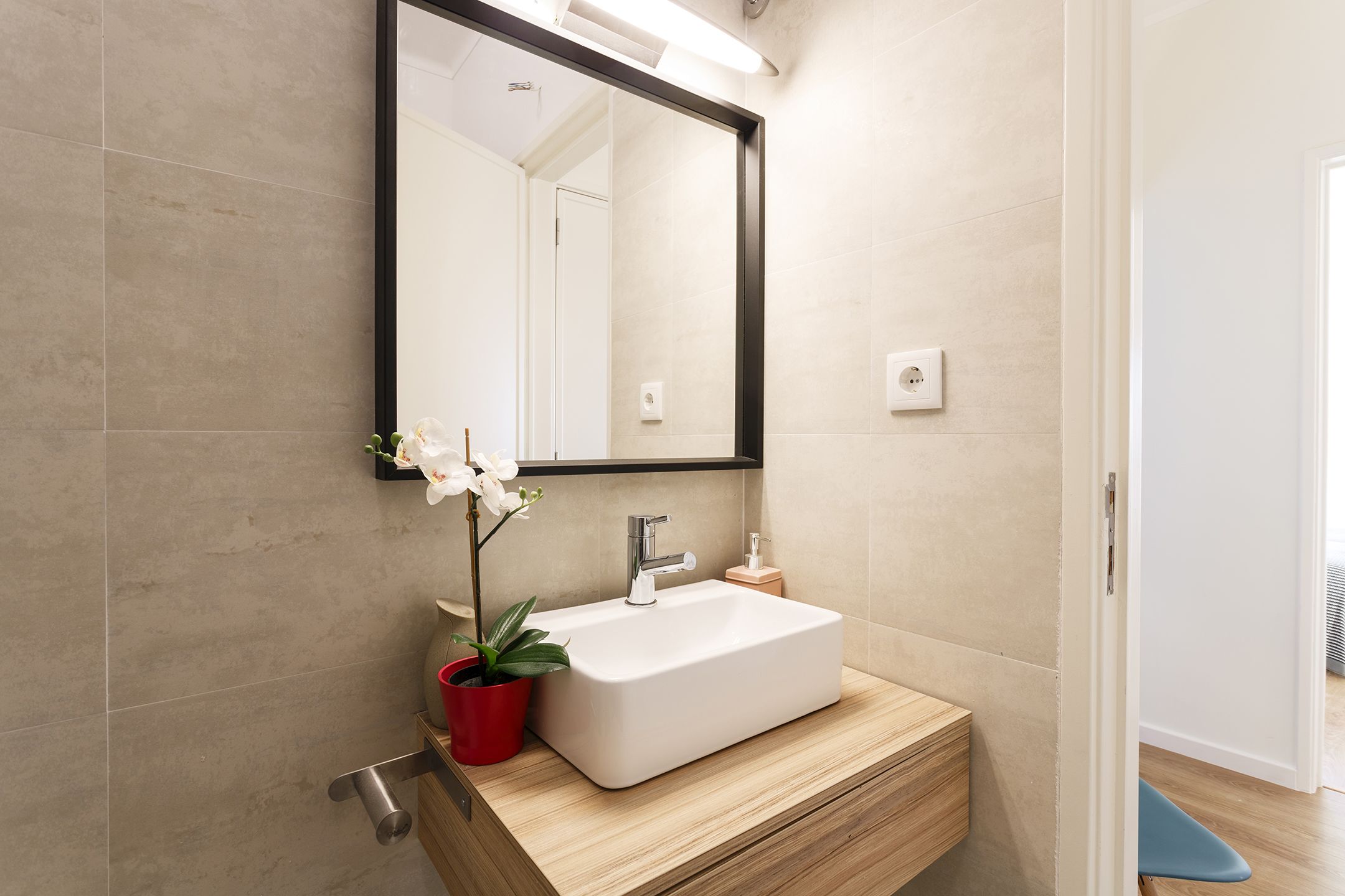 A modern bathroom with a rectangular sink, a large mirror, and a potted orchid.