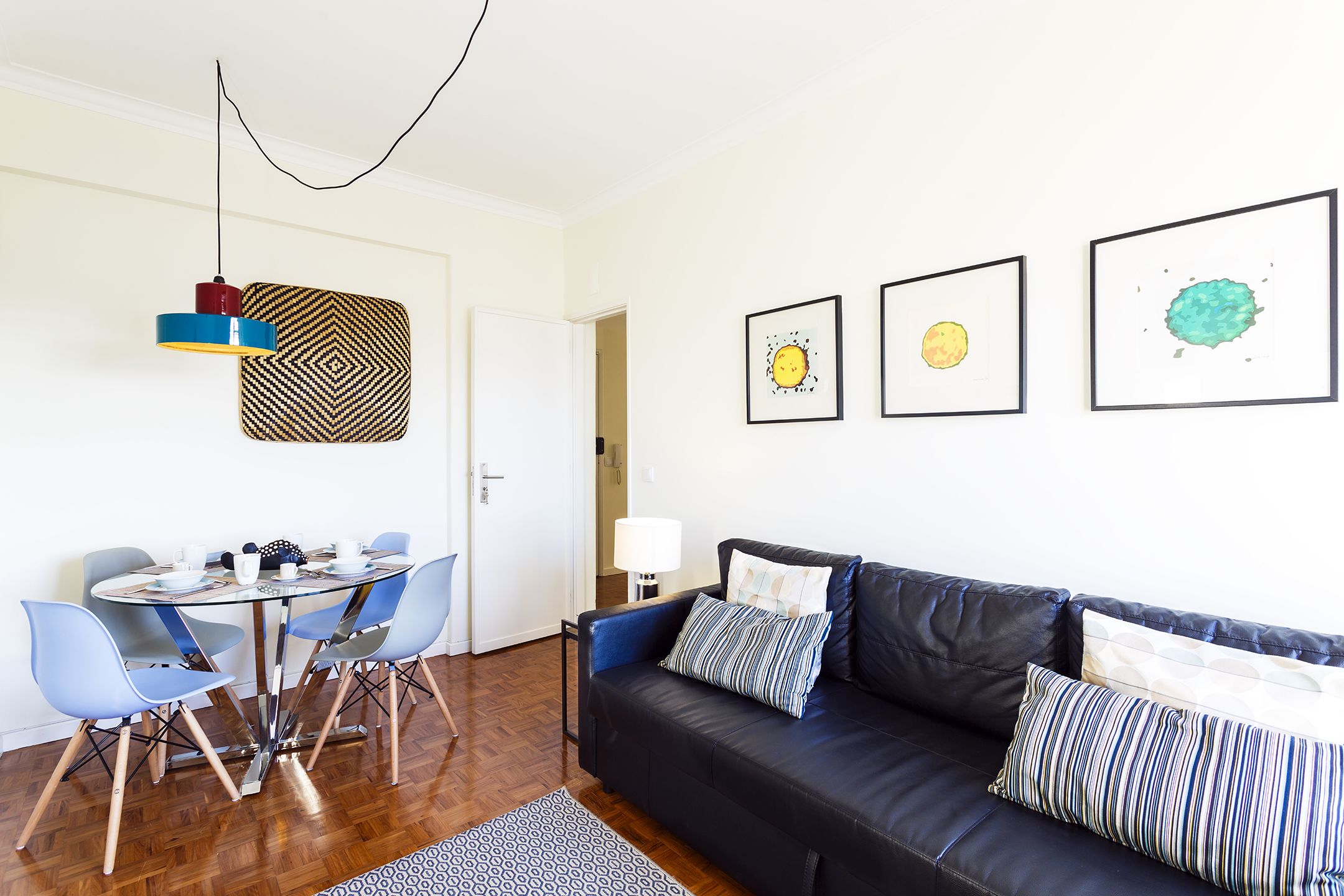 Un soggiorno moderno con un divano in pelle nera, poltrone blu, un tavolo da pranzo in vetro e un pannello decorativo a parete.