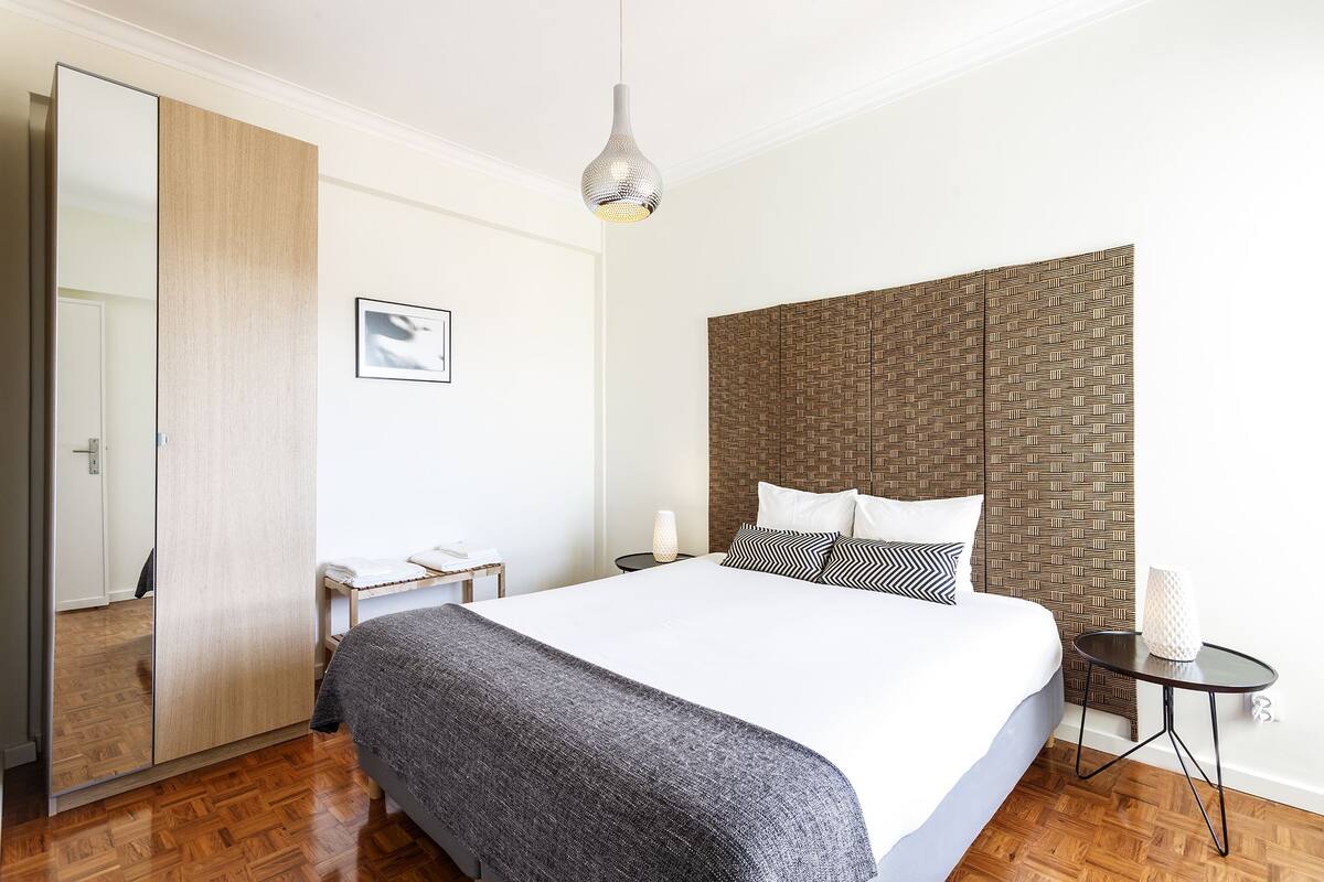 Ein modernes Hotelzimmer mit einem großen Bett, einem Nachttisch, einem Spiegel und einem gemusterten Kopfteil.