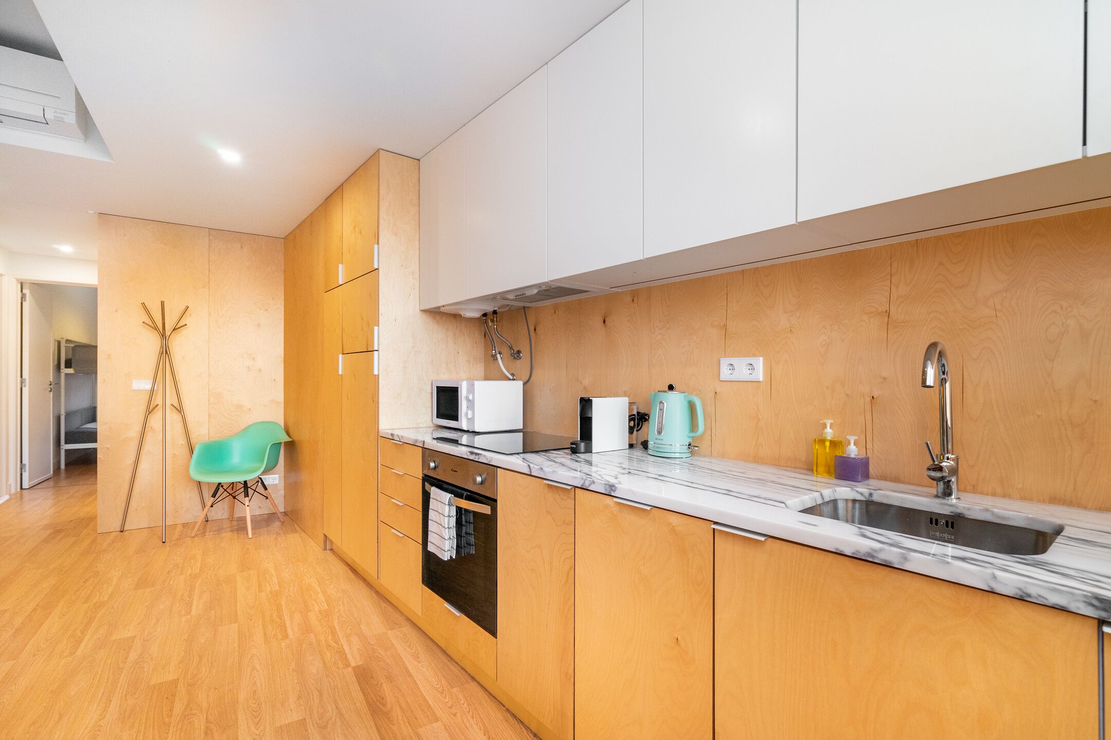 Une cuisine moderne avec des meubles en bois, un plan de travail en marbre, un évier, un four à micro-ondes, une bouilloire et une chaise de couleur turquoise.