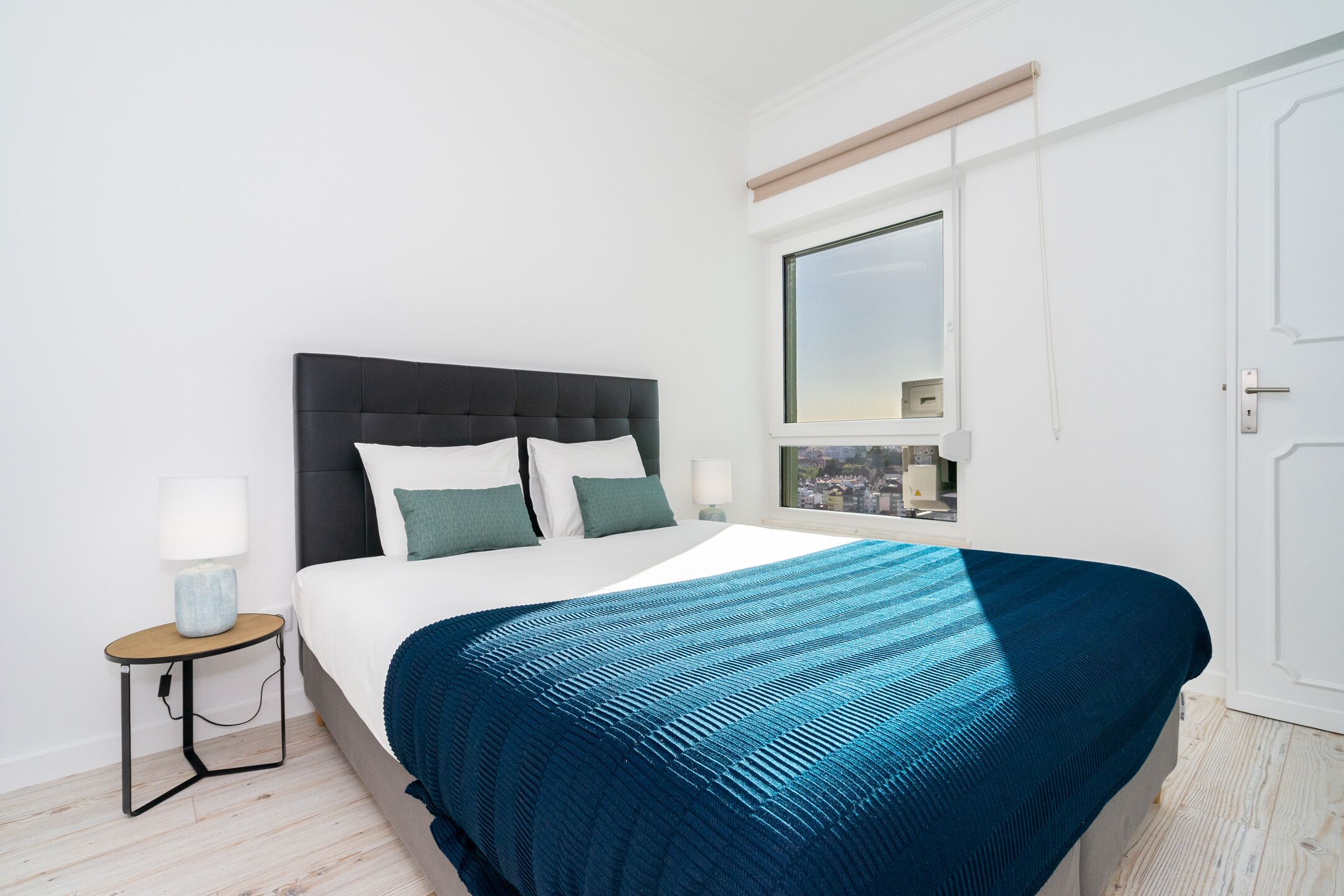 A bedroom with a bed, a nightstand, a window, and a door.
