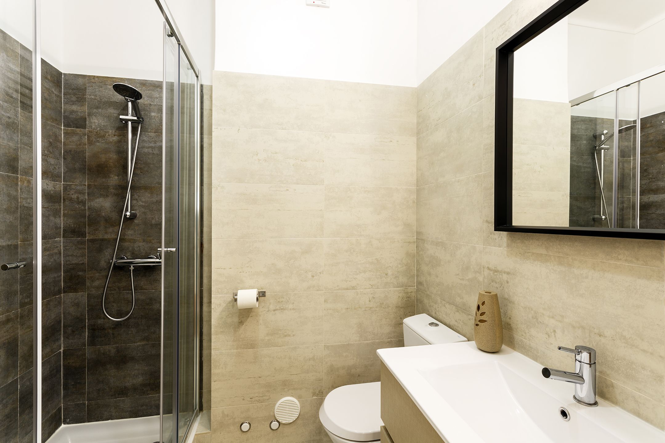 A modern bathroom with a glass-enclosed shower, a white sink, and a beige toilet.