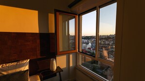 Una habitación de hotel con un ventanal grande, una cama, una mesita de noche y un espejo.
