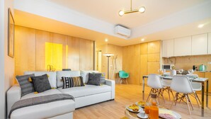 Una sala moderna con un sofá blanco, comedor con sillas y una cocina al fondo.