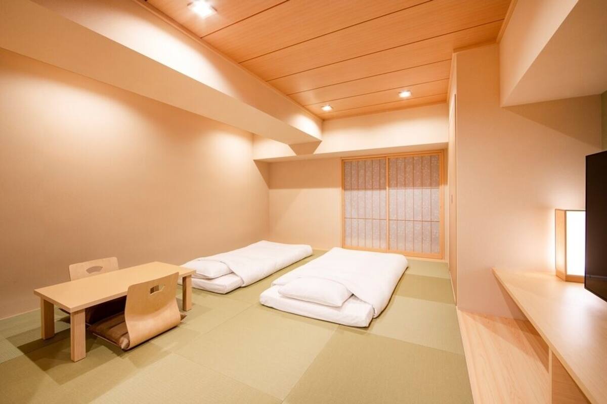 A room with a wooden ceiling, two beds, a small table, and a TV.