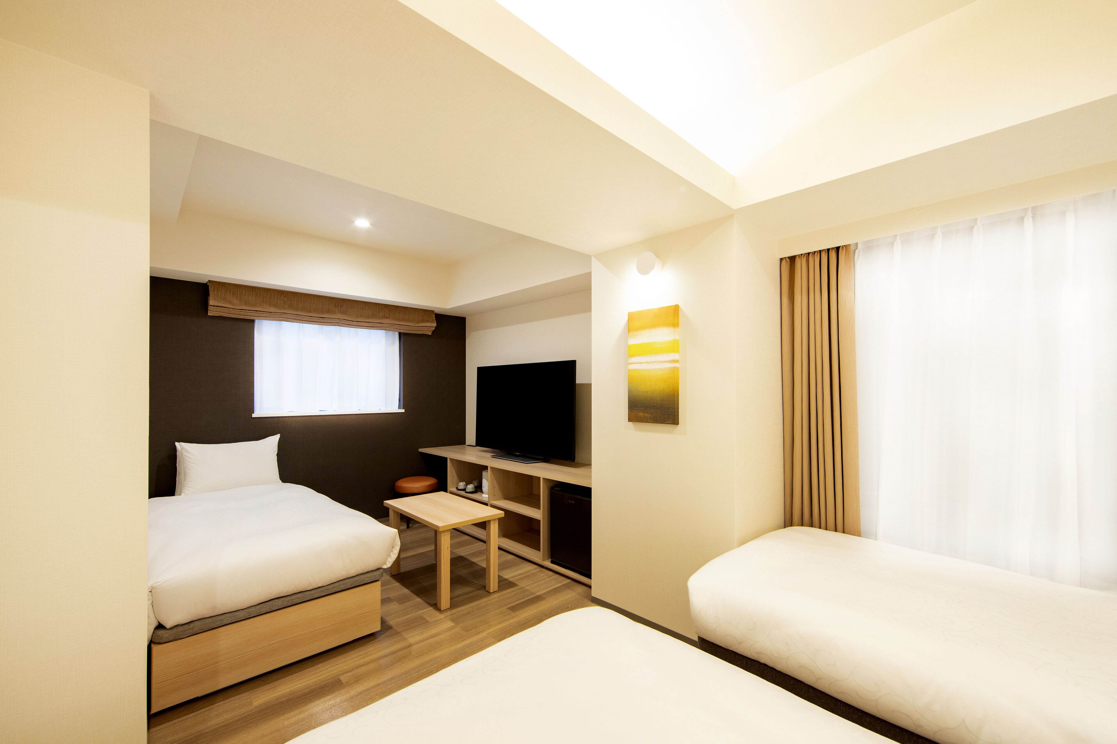 A hotel room with two beds, a TV, a small table, and a window with curtains.