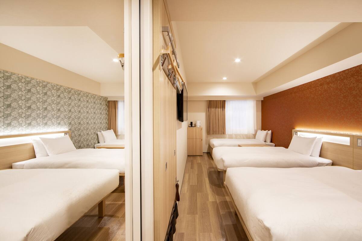 A hotel room with three beds, a wooden floor, a patterned wall, and a mirror.