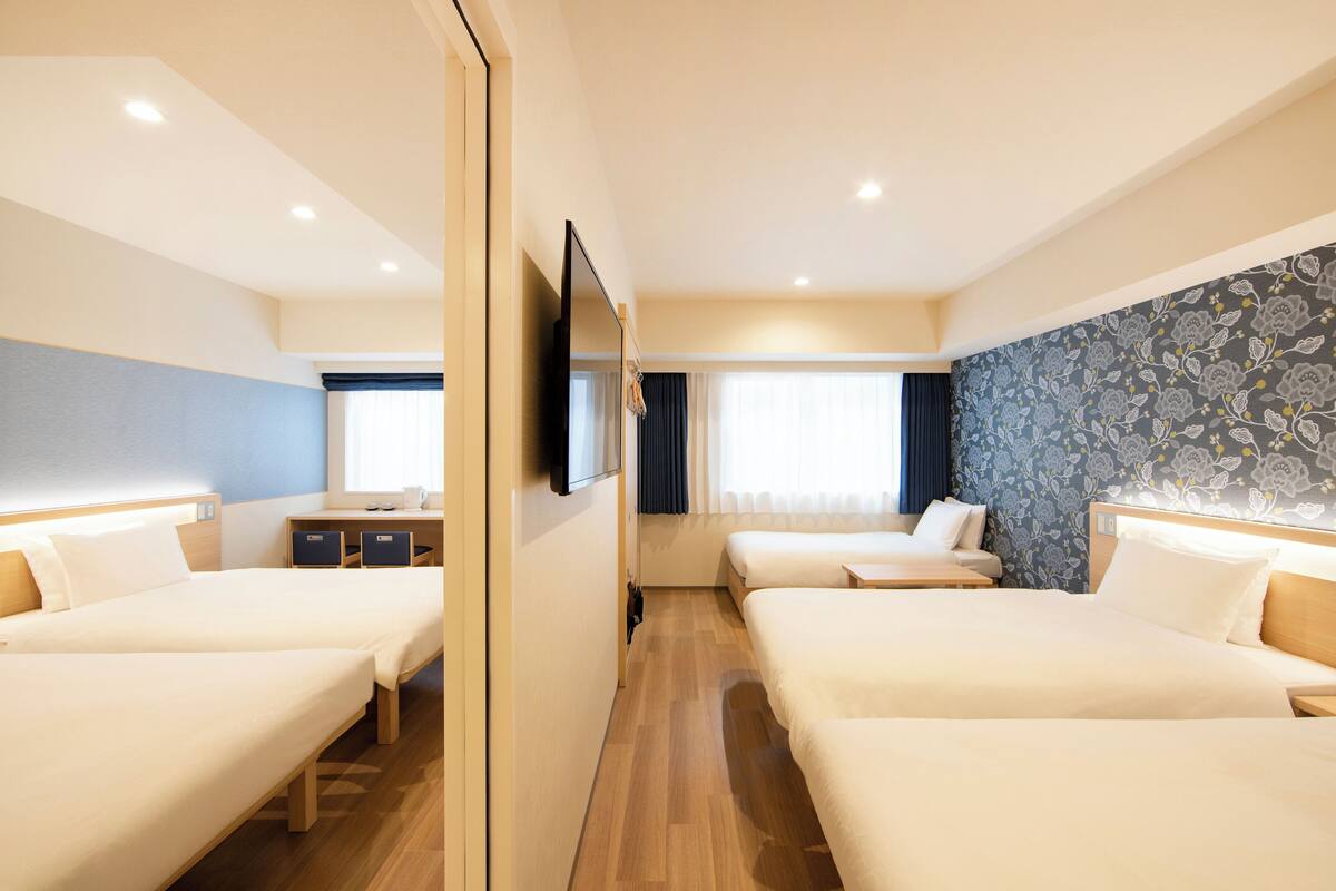 A hotel room with three beds, a desk, and a TV.
