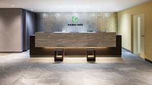 A reception desk with a marble-like wall and a logo above it. - karaksa hotel TOKYO STATION (Tokyo)