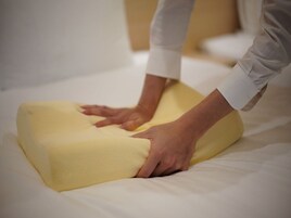 Une personne est en train de disposer un oreiller jaune sur un lit.