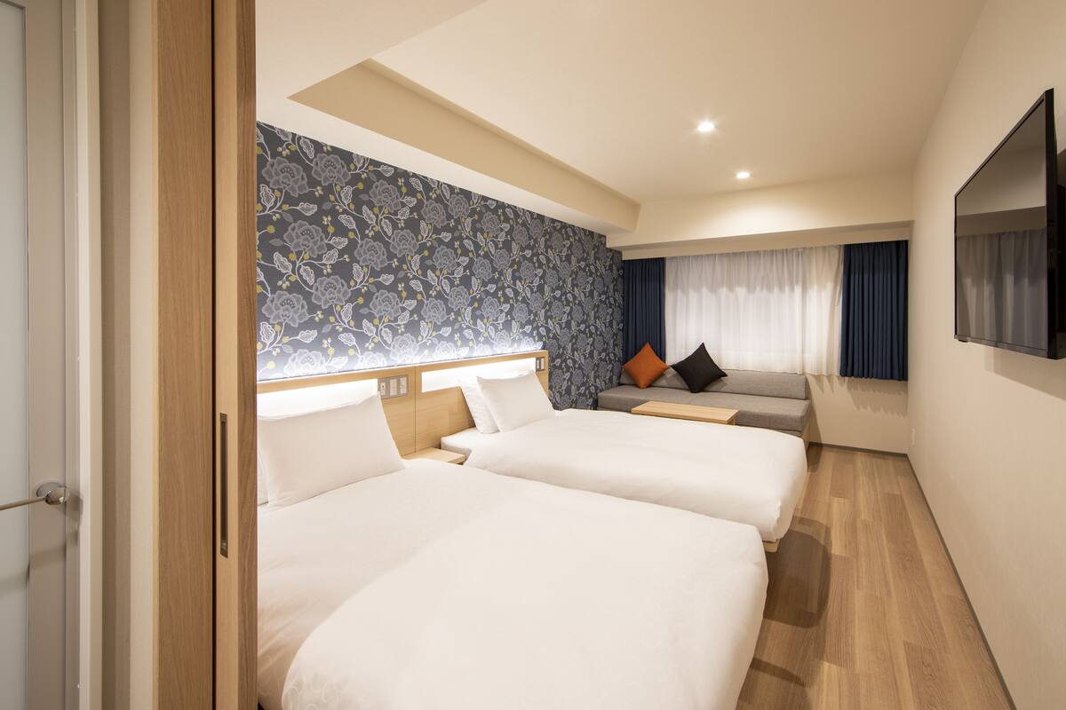 A hotel room with two beds, a sofa, a TV, and a patterned wall.