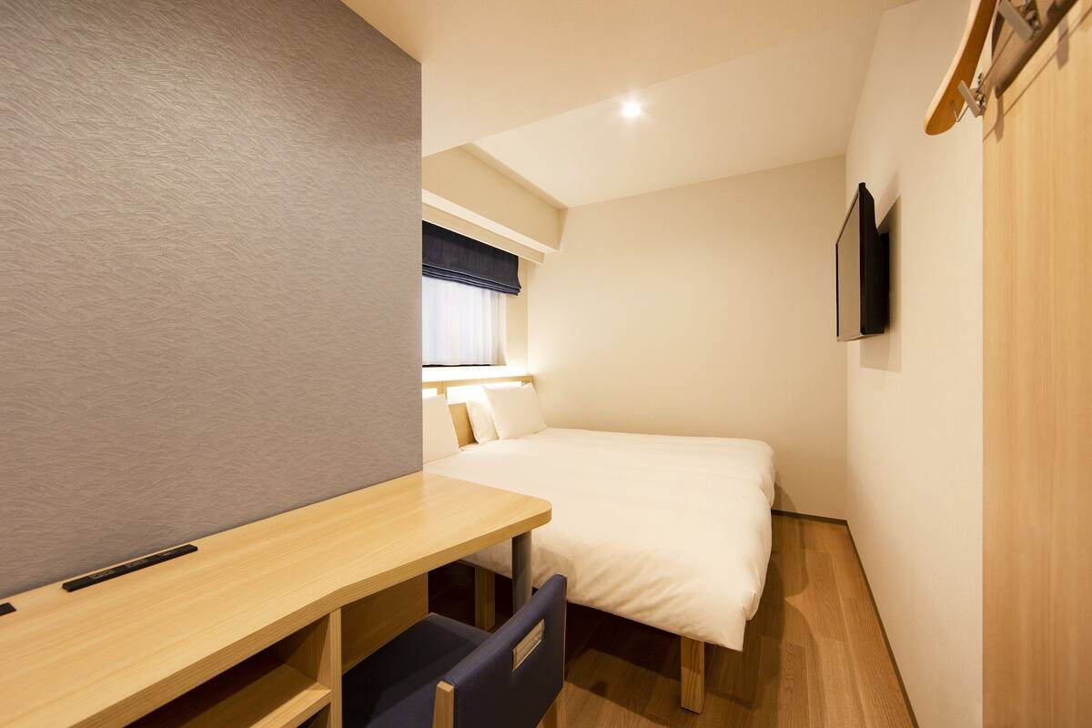 A compact hotel room with a single bed, a desk, and a television mounted on the wall.