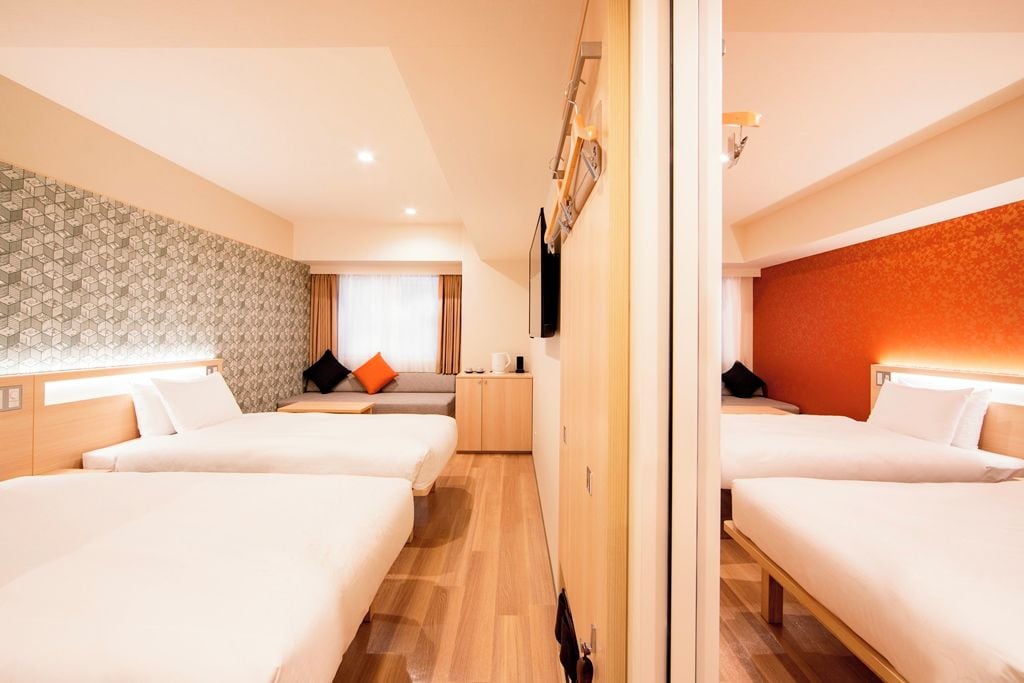 Una habitación de hotel con dos camas, un sofá, un televisor y una pequeña kitchenette.