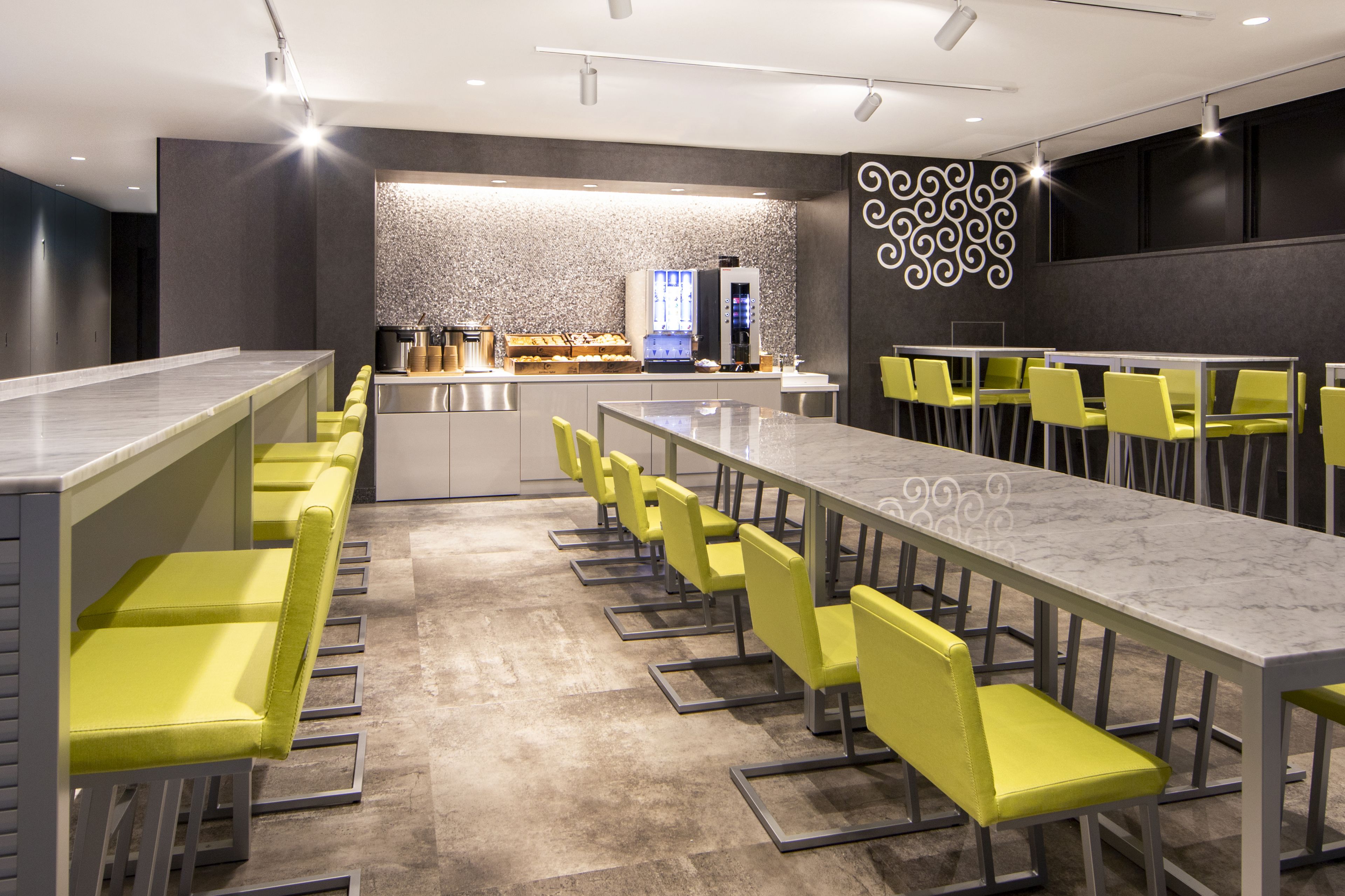 A modern restaurant with a long counter and yellow chairs, a bar area, and a decorative wall.