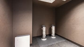 A restroom with two trash bins, a white air conditioning unit, and a grey mat on the floor.