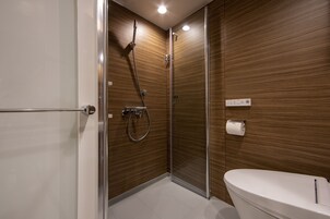 A modern bathroom with a glass-enclosed shower, a white toilet, and wooden paneling on the walls.