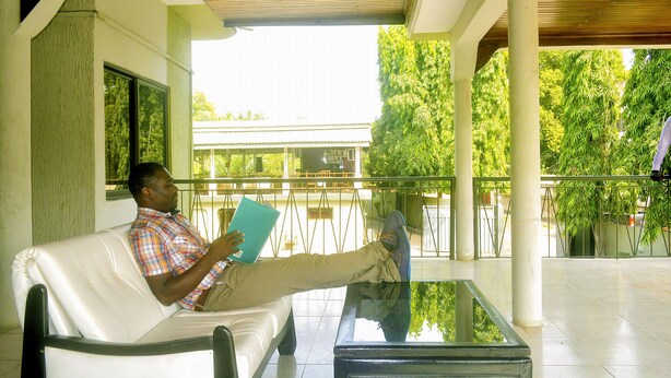 Un hombre sentado en un sofá de cuero blanco con una mesa de vidrio frente a él, leyendo un libro.
