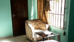 Una habitación con cama, una silla, una ventana con cortinas y una puerta.