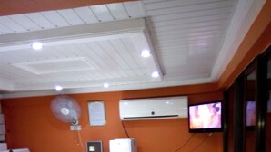 Un área de recepción con un mostrador blanco, un equipo de aire acondicionado, un televisor montado en la pared y un ventilador.