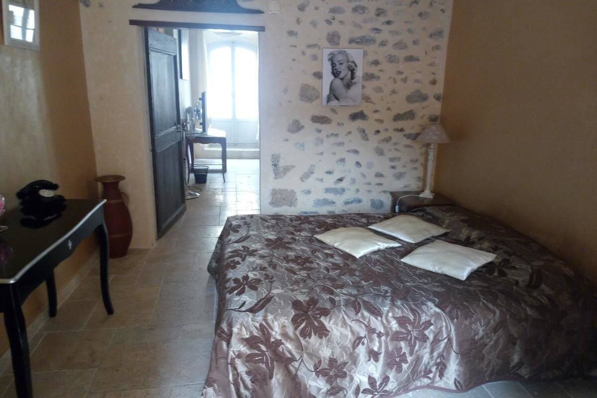 Ein Schlafzimmer mit einem Bett, einem Schreibtisch und einem Stuhl. Eine Tür führt in einen anderen Raum.